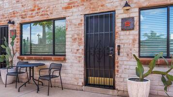 A brick building with a black metal gate, a small patio with two chairs, and a cactus plant.
