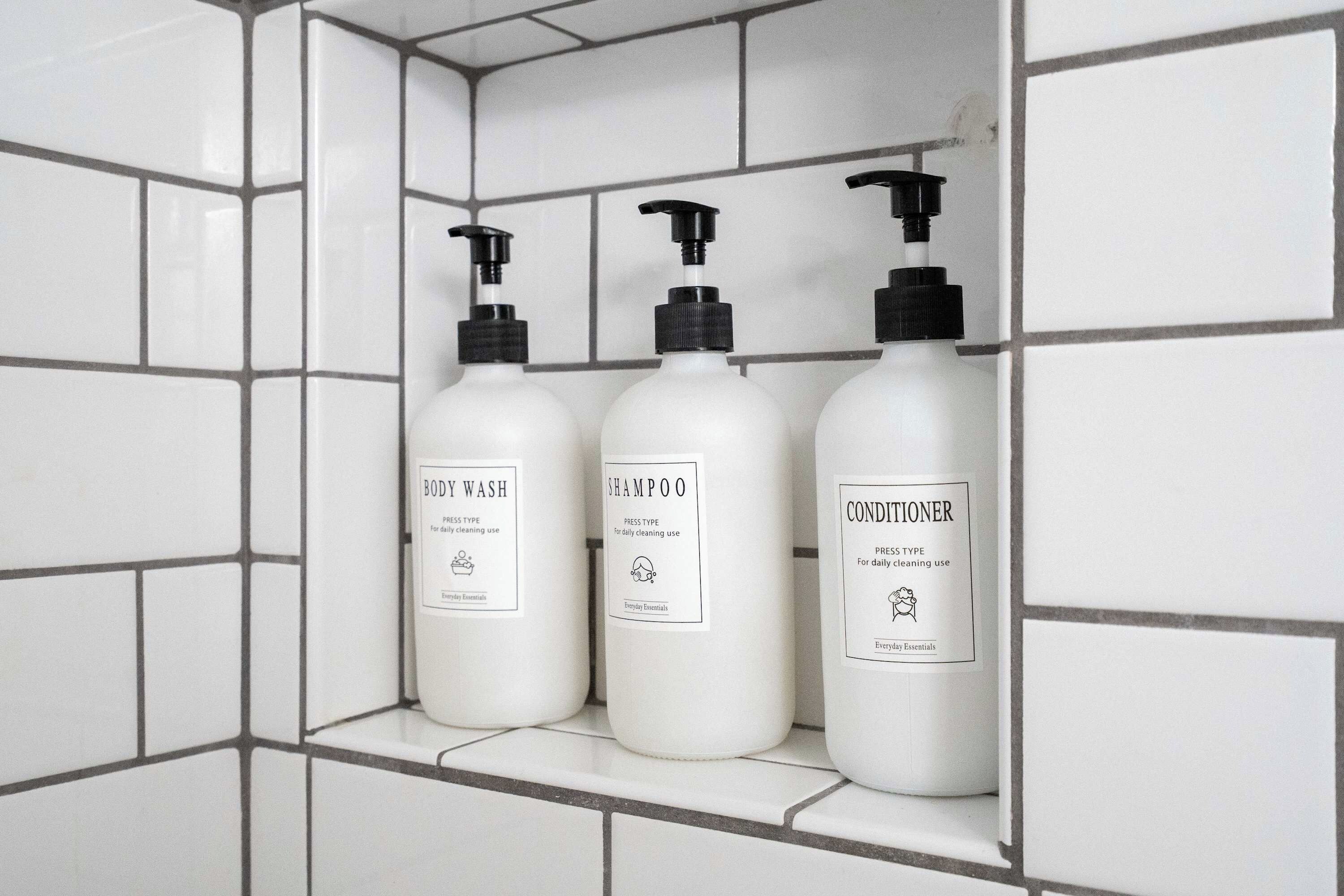 Three bottles of toiletries on a shelf in a tiled bathroom.
