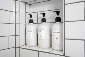 Três frascos de produtos de higiene pessoal numa prateleira em um banheiro com azulejos.