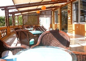 An outdoor patio with wicker furniture and glass tables, a wooden pergola, and a view of the surrounding area. - Siesta Marina Hotel (Al-Hammam)