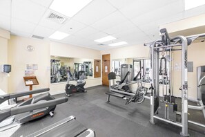 Ett gym med träningsredskap, ett löpband och en spegel på väggen.
