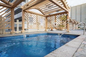 Ett poolområde med en pergola av trä, en skylt som visar att en badvakt är i tjänst och en markering som anger poolens djup.