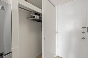 En vit dörr med lås och handtag, en garderob med upphängda kläder och ett kylskåp.