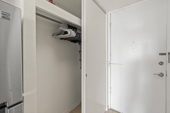 A white door with a lock and a handle, a closet with hanging clothes, and a refrigerator. - Cozy 1-bedroom condo with AC in Waikiki (Honolulu)