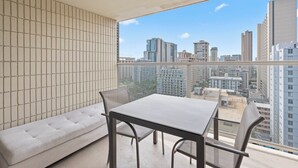 A balcony with a city view, a sofa, and a table with chairs. - Cozy 1-bedroom condo with AC in Waikiki (Honolulu)