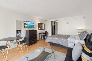 A modern bedroom with a bed, a desk, and a chair. There is a painting on the wall and a window. - Cozy 1-bedroom condo with AC in Waikiki (Honolulu)