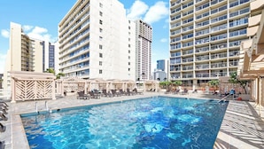 A swimming pool with lounge chairs and umbrellas, surrounded by high-rise buildings. - Cozy 1-bedroom condo with AC in Waikiki (Honolulu)