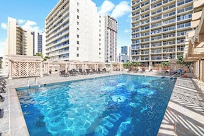 A swimming pool with lounge chairs and umbrellas, surrounded by high-rise buildings. - Cozy 1-bedroom condo with AC in Waikiki (Honolulu)