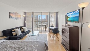 A modern living room with a sofa, a coffee table, a TV, and a balcony with a city view. - Cozy 1-bedroom condo with AC in Waikiki (Honolulu)