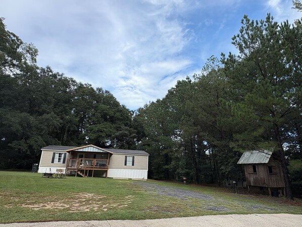 A single-story house with a porch and a small shed in a wooded area.