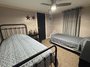 A bedroom with two beds, a ceiling fan, a nightstand with a clock and a small ship model, and a door with a star decoration.