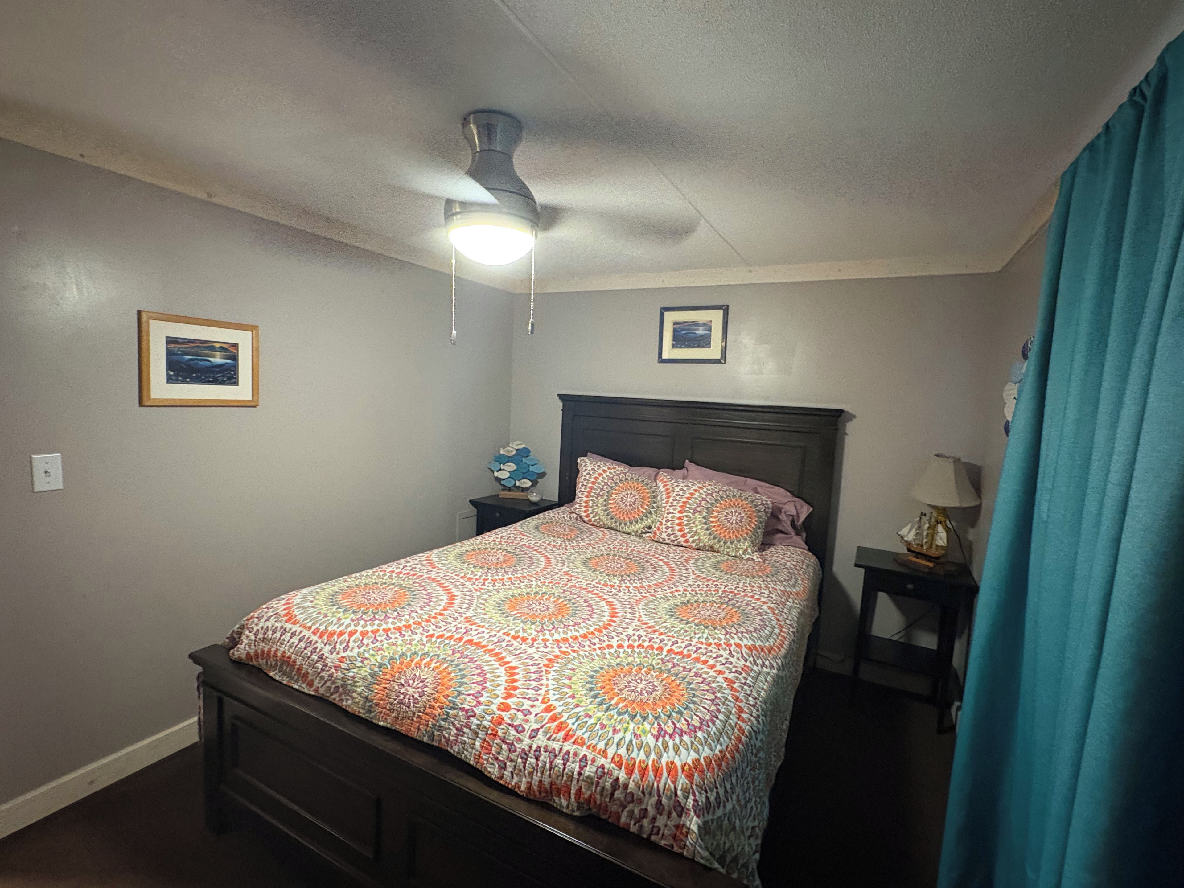 A bedroom with a bed, a nightstand, a ceiling fan, and two framed pictures on the wall.