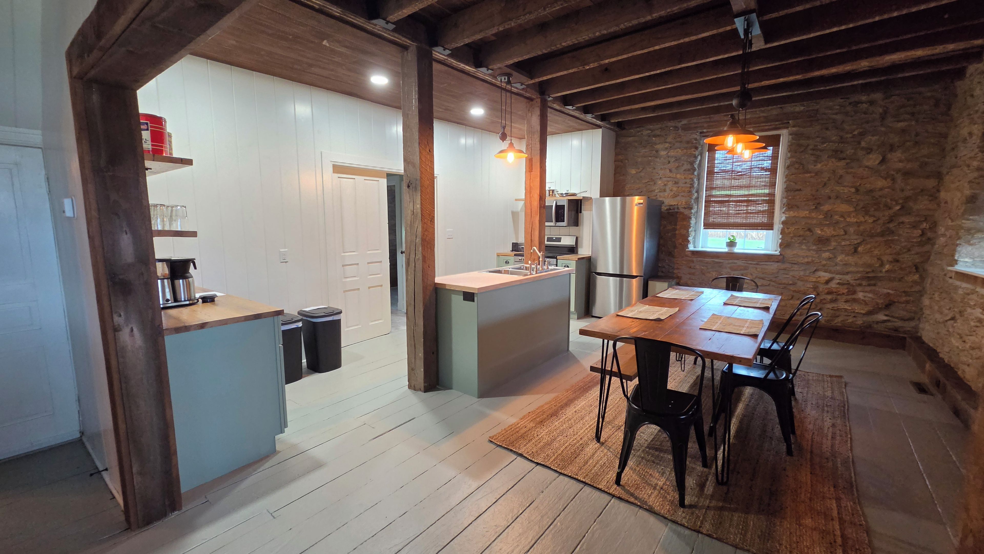A compact kitchen with a central island, wooden beams, stone walls, and a dining area with a table and chairs.