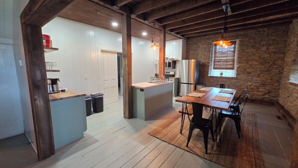 A compact kitchen with a central island, wooden beams, stone walls, and a dining area with a table and chairs.