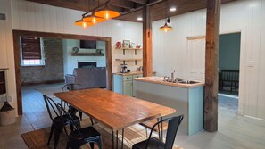 Een eetgedeelte met een houten tafel en stoelen, een keuken met een spoelbak en kasten, en een stenen muur.