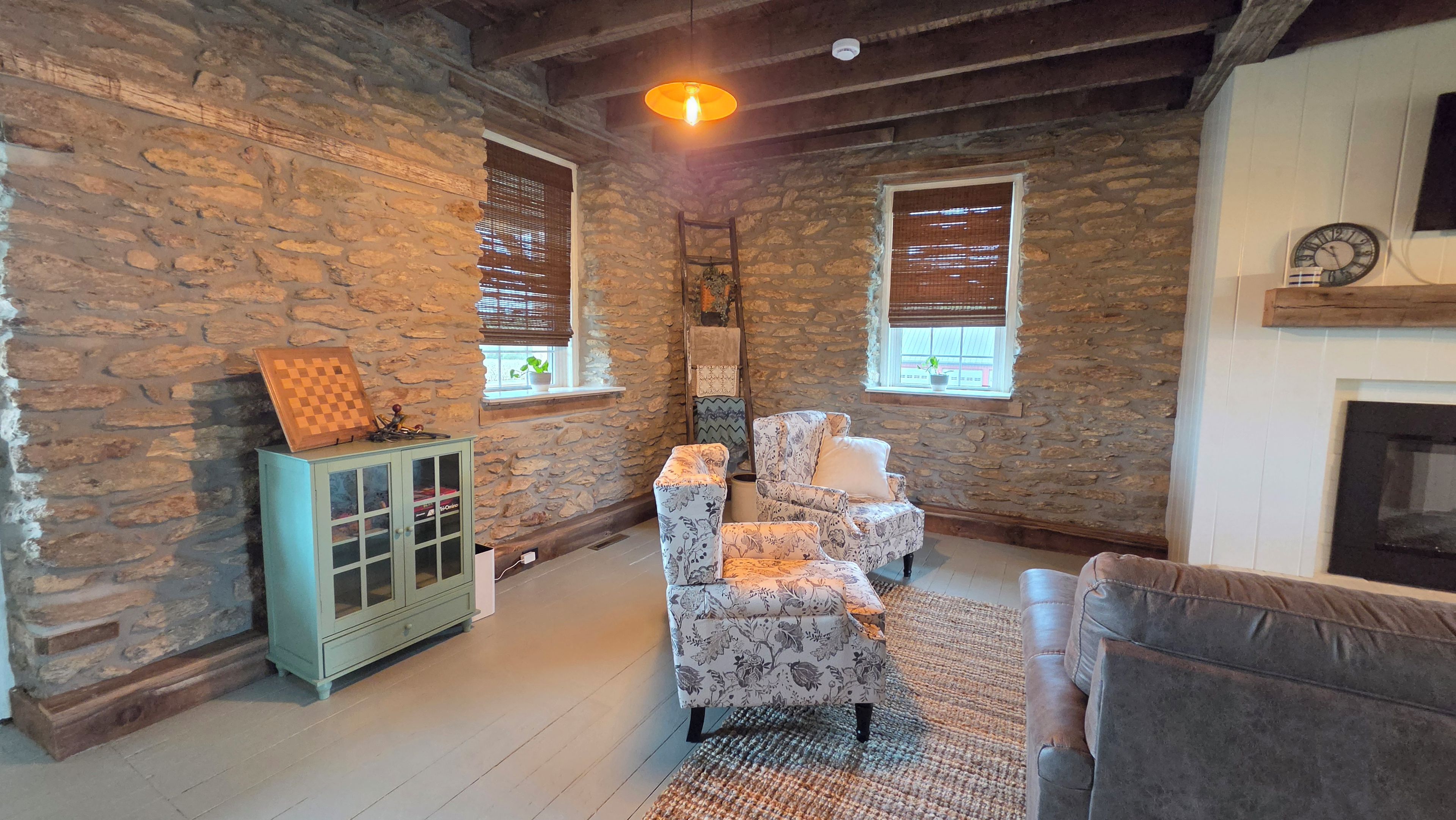 A room with stone walls, a wooden cabinet, a patterned armchair, a sofa, and a fireplace.
