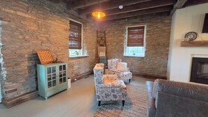A room with stone walls, a wooden cabinet, a patterned armchair, a sofa, and a fireplace.