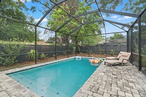 A covered outdoor swimming pool with a patio area, surrounded by a fence and vegetation. - Heated Pool Getaway In Tampa Bay, Sleeps, Close to everything in Tampa Bay! (Tampa)