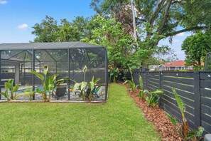 Una estructura de hivernacle amb teulada transparent, envoltada per un jardí amb gespa i una tanca de fusta.