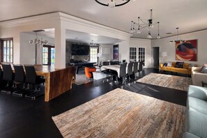 Een ruime woonkamer met een eettafel, meerdere stoelen, een bank en een groot vloerkleed.