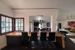 A modern kitchen with a large island, black chairs, and a dining area with a view of the outdoors. - Private Villa w/ Pool, Spa, Gym, Sauna, Spectacular Backyard, & 2 miles to Strip (Las Vegas)