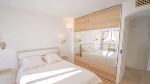 Quarto moderno com cama grande, espelho e vista para uma varanda.