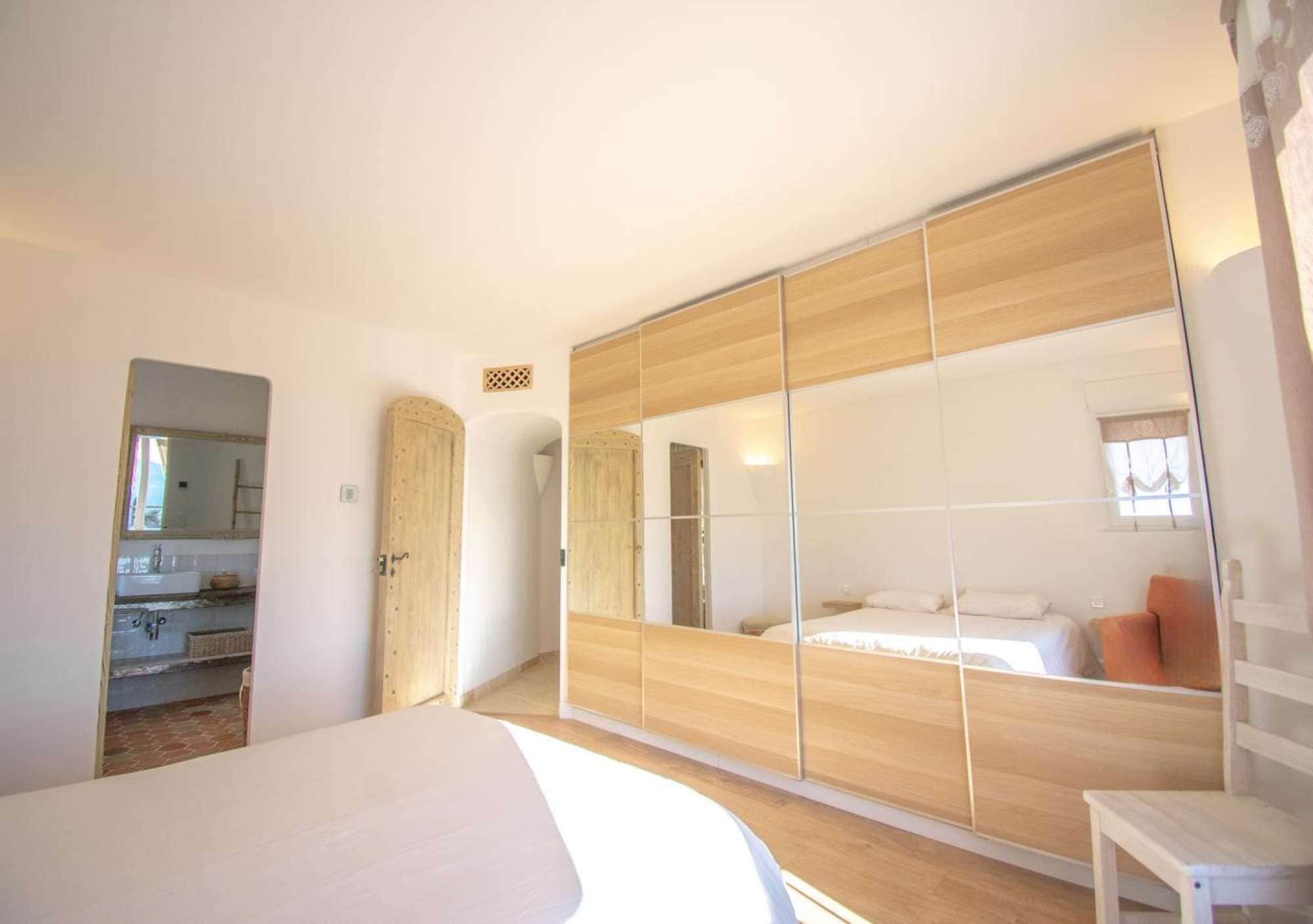 A bedroom with a large mirror, wooden wardrobe, and a bed.