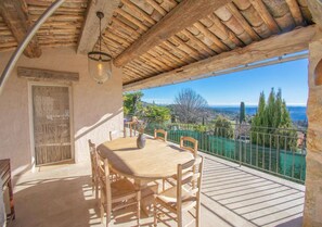 A wooden table and chairs on a balcony with a view of the sea and greenery. - Cabris, Mas provençal 6p, 3ch, AC, piscine, vue (Cabris)