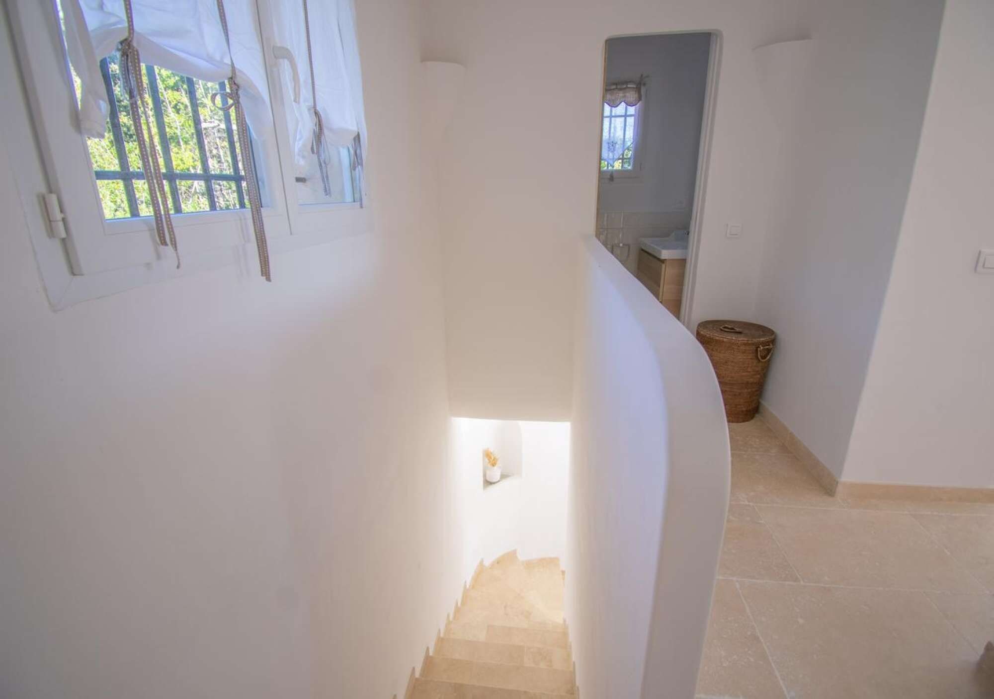 A staircase leading to a lower level, a window with curtains, and a small potted plant.