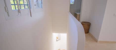 A staircase leading to a lower level, a window with curtains, and a small potted plant.