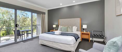 A modern hotel room with a large bed, a balcony with outdoor seating, and a view of trees.