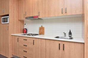 A modern kitchen with wooden cabinets, a microwave, a kettle, a gas stove, and a sink. - Duck Pond Villa at Hunter Valley Golf Resort Views (Lovedale)