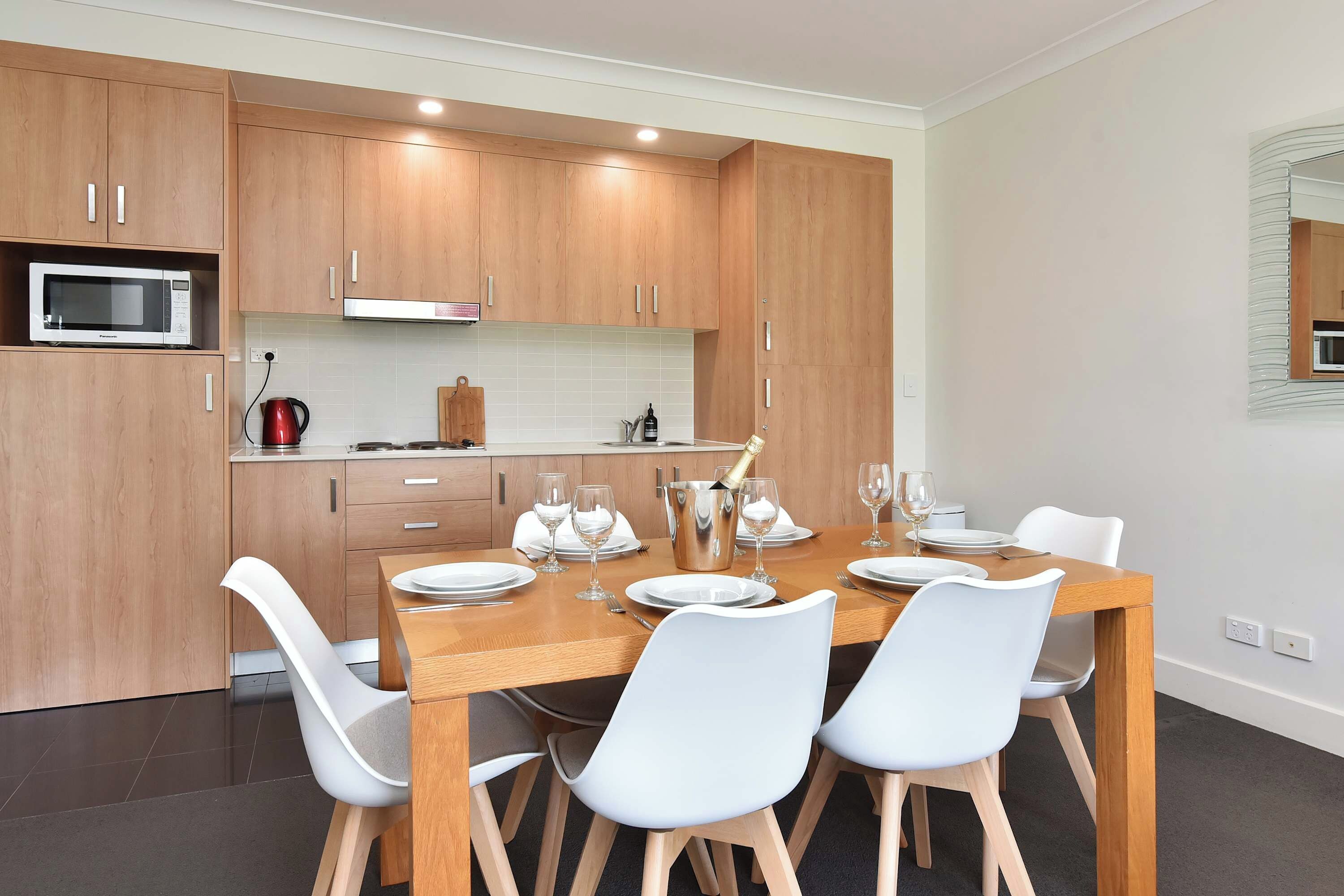Une cuisine moderne avec des meubles en bois, un four à micro-ondes encastré et un coin repas comprenant une table en bois et des chaises blanches.