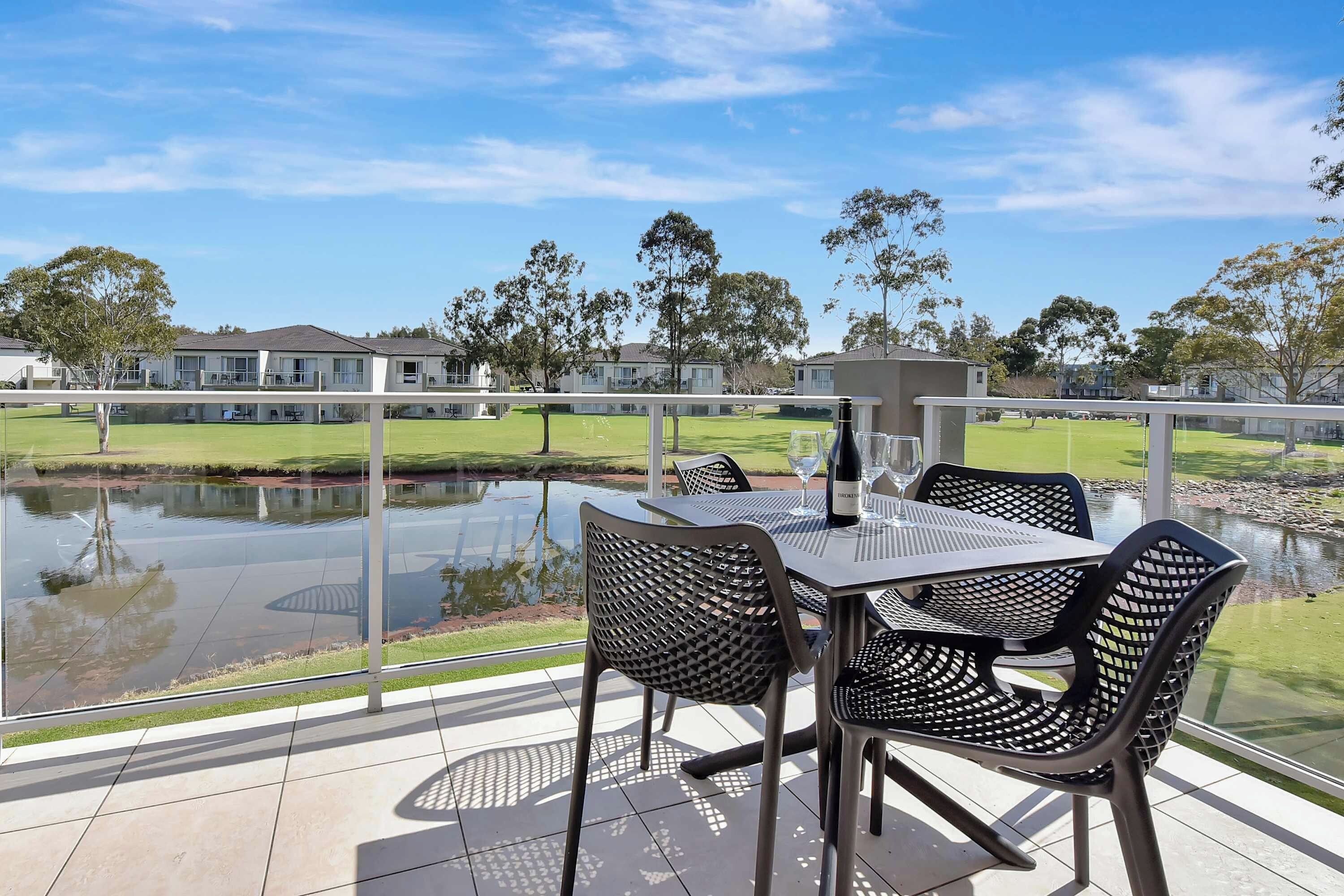 An outdoor patio with a table and chairs, a pond, and a view of residential buildings.