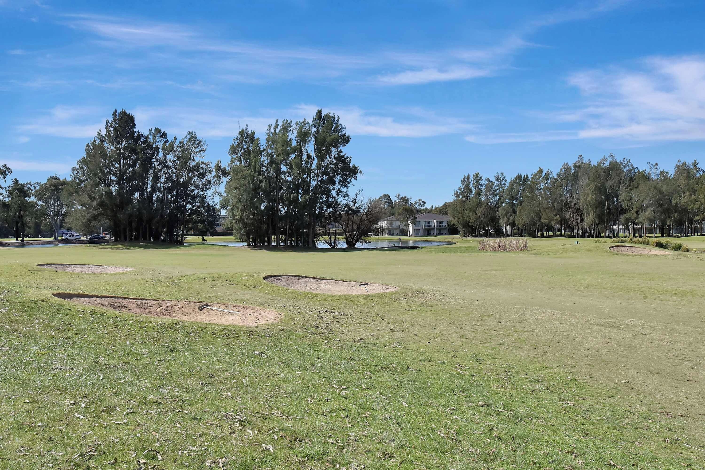 A golf course with sand bunkers, trees, and a clear sky.