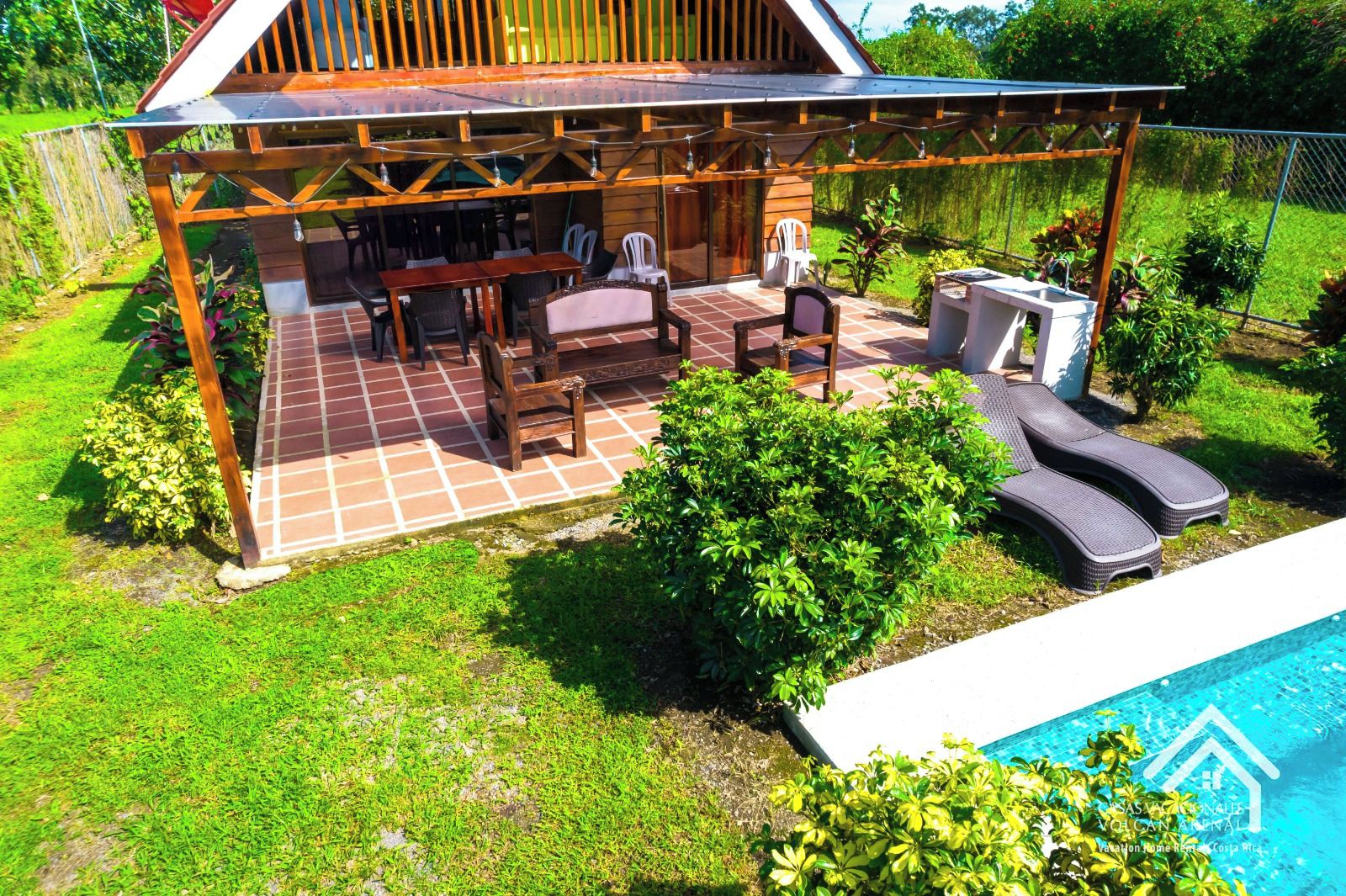 Un espace extérieur aménagé, abrité et doté de tables et de chaises, ainsi qu’une piscine et une végétation luxuriante.