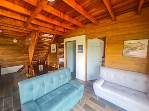 A wooden interior with a dining table, two sofas, and a staircase.