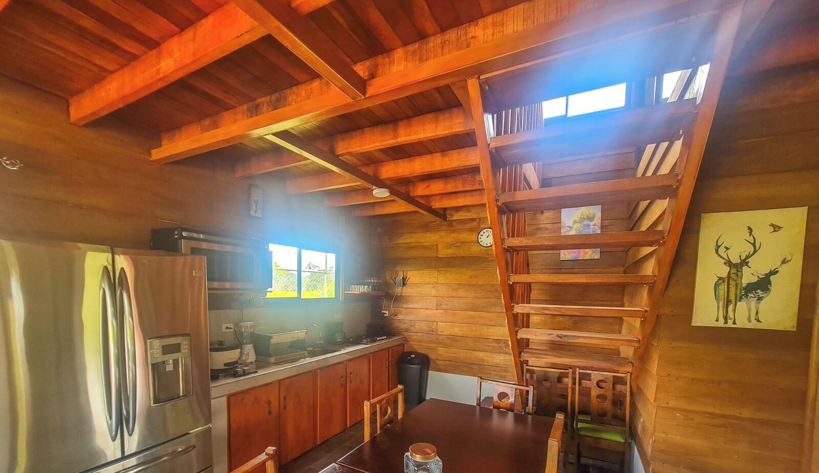 A rustic kitchen with wooden beams, a stainless steel refrigerator, and a wooden staircase.