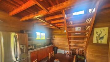 A rustic kitchen with wooden beams, a stainless steel refrigerator, and a wooden staircase.