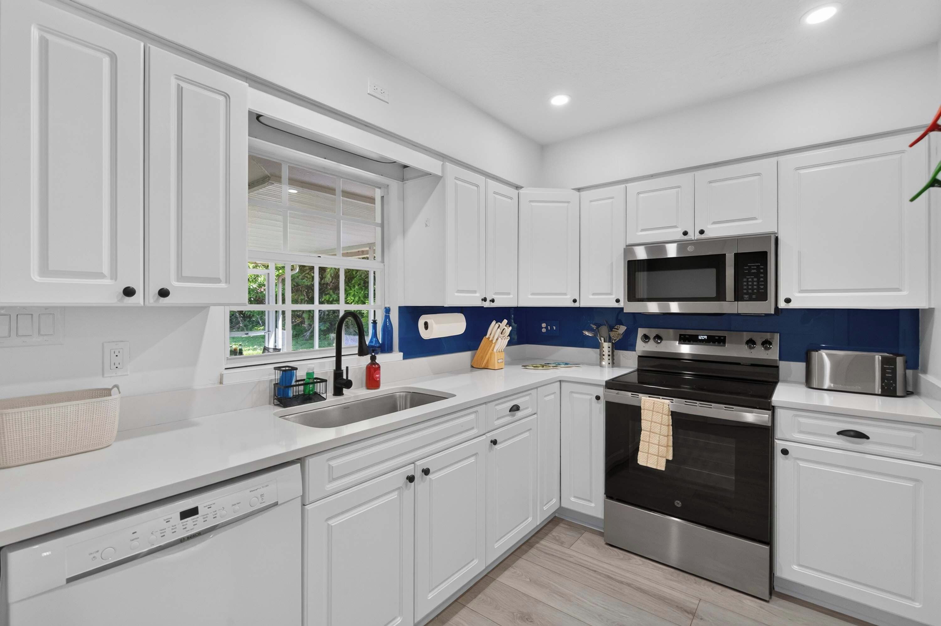 A modern kitchen with white cabinetry, stainless steel appliances, and a blue backsplash.