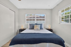 Ein Schlafzimmer mit einem Bett, zwei Nachttischen, einem Fenster und Blick nach draußen.
