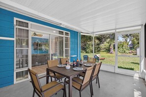 Un porche cubierto con una mesa dispuesta para cuatro personas, rodeado de sillas y vistas a un jardín.