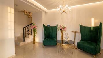 Una sala de estar moderna con una escalera, sillones de terciopelo verde, una mesa redonda de centro y una araña.