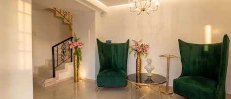 A modern living room with a staircase, green velvet armchairs, a round coffee table, and a chandelier.