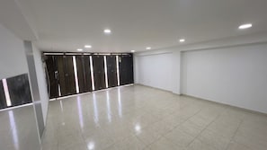 Una habitació àmplia amb terra de rajola, una porta amb marc negre i il·luminació encastada al sostre.