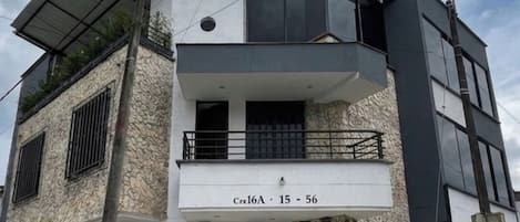A modern two-story building with a flat roof, a balcony on the upper floor, and a ground-level entrance.
