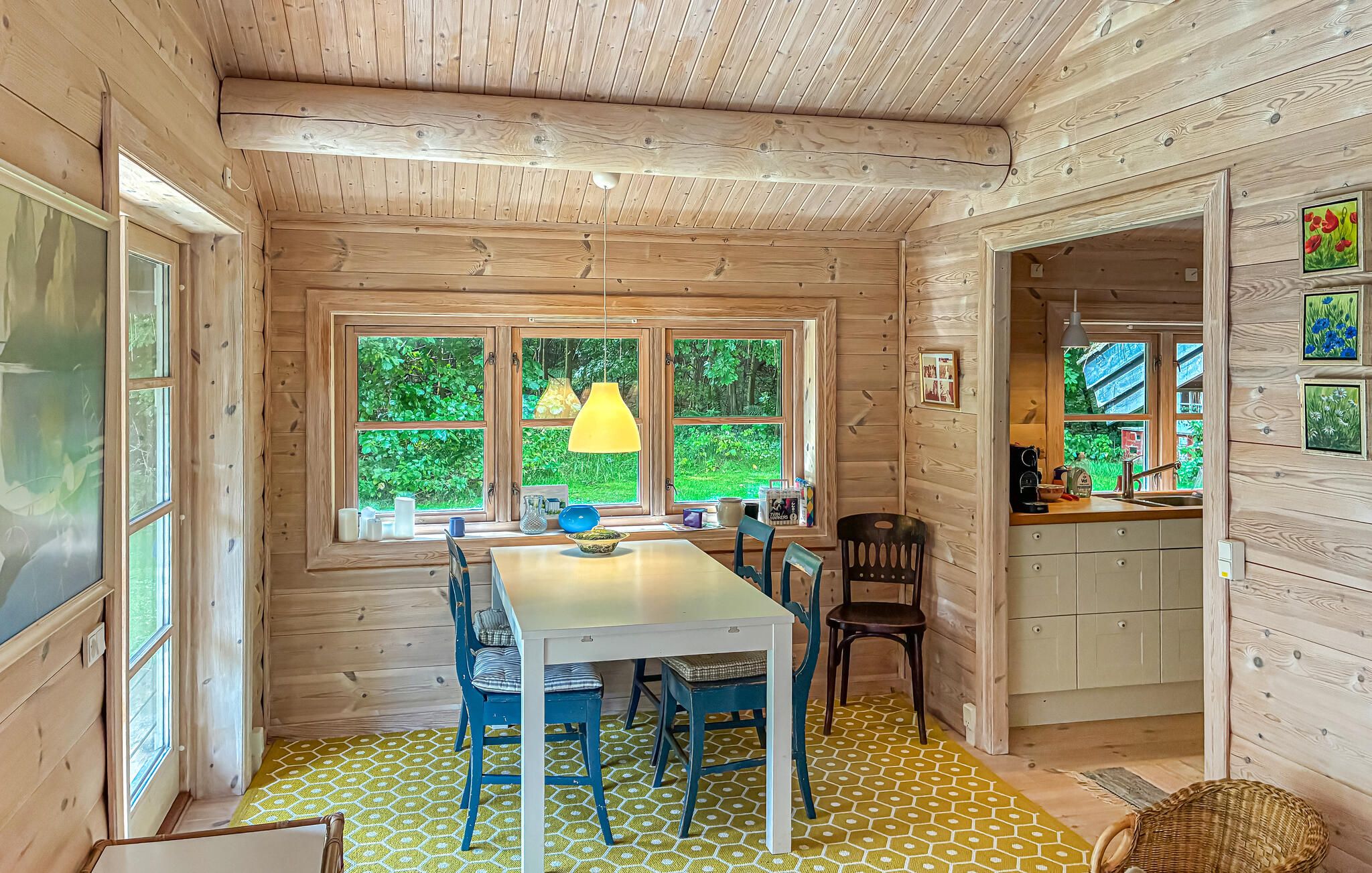 A wooden interior with a dining table, chairs, and a window with a view of greenery.