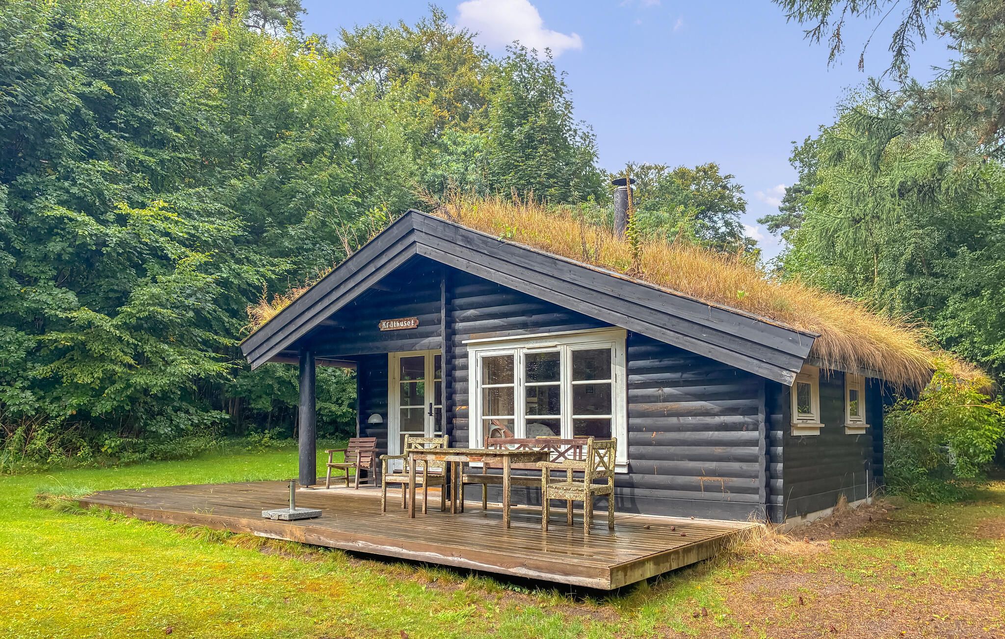 Una cabaña de troncos con techo de paja, una terraza con mobiliario exterior y un letrero que dice 'Krathuset'.