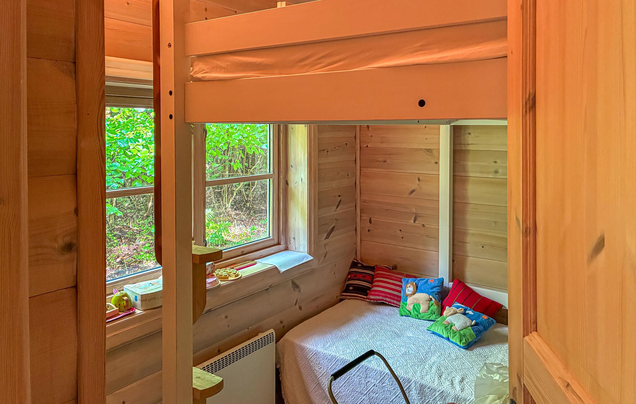 Una cama litera infantil con ventanal, una mesita con juguetes y una cama con almohadas coloridas.