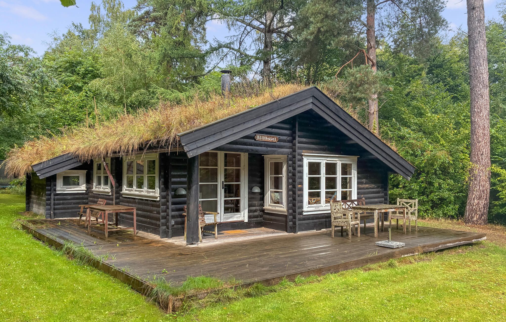 A log cabin with a thatched roof, wooden deck, and a sign reading 'Krathuset.'